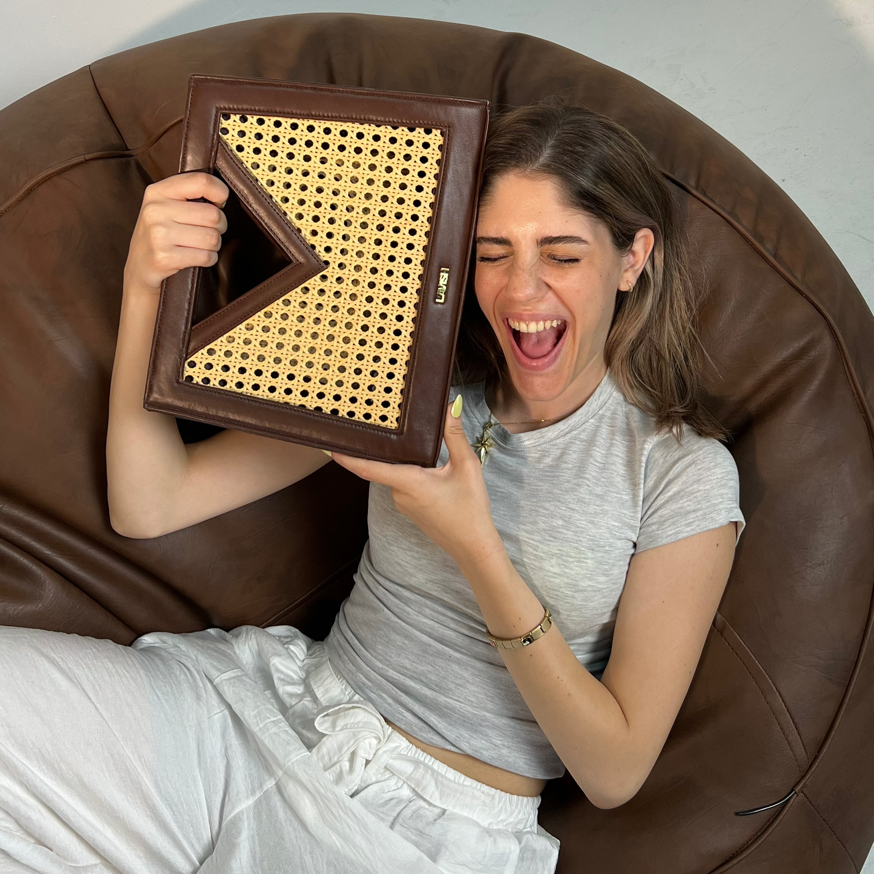 Woman sitting on a brown bean bag chair holding a woven frame.